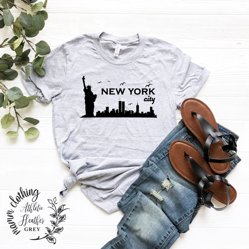 May include: A gray t-shirt with a black graphic of the Statue of Liberty and the New York City skyline. The text "NEW YORK city" is printed on the shirt.