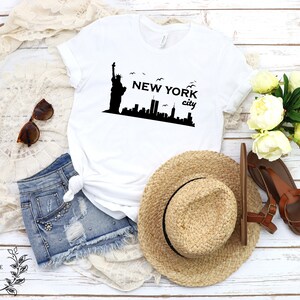 May include: White t-shirt with a black graphic of the Statue of Liberty and the New York City skyline. The text "NEW YORK city" is printed below the graphic.