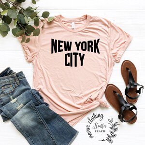 May include: A light pink t-shirt with black text that reads "NEW YORK CITY".