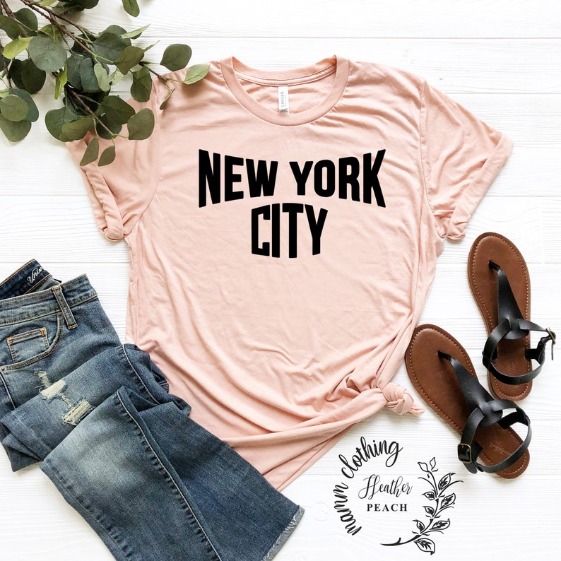 May include: A light pink t-shirt with black text that reads "NEW YORK CITY".