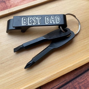 May include: Black metal bottle opener keychain with a screwdriver and a small flathead screwdriver. The bottle opener has the words "BEST DAD" engraved on it.