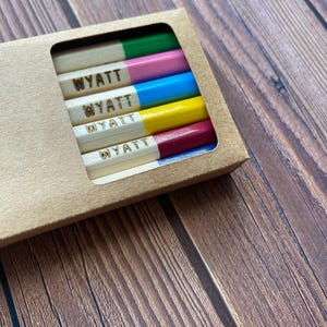 以下が含まれることがあります： 「WYATT」と刻印された木製の鉛筆が5本セットになっています。鉛筆は緑、ピンク、青、黄、赤茶色の異なる色で塗られています。