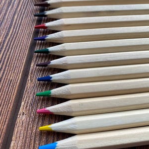 以下が含まれることがあります： 赤、青、緑、黄、茶色など、さまざまな色の木製のカラー鉛筆12本セット。鉛筆は一列に並べられ、先端が視聴者の方を向いています。