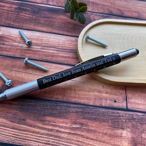 May include: A black multi-tool pen with a silver tip and a personalised inscription that reads "Best Dad, love from Amelia and Ted x".