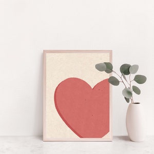May include: A framed print of a simple, minimalist design featuring a large, coral-colored heart on a cream background.