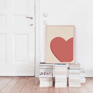 May include: A framed print of a large, red heart on a cream background. The print is leaning against a stack of books.