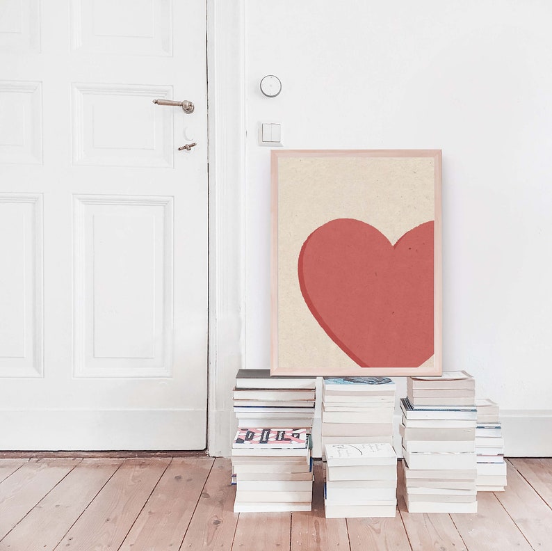 May include: A framed print of a large, red heart on a cream background. The print is leaning against a stack of books.
