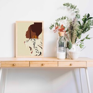 Pu&ograve; includere: Una stampa incorniciata di un'illustrazione digitale di una donna con una tigre bianca. La donna ha la pelle marrone e un orecchino a cerchio dorato. La tigre &egrave; bianca con strisce nere. Lo sfondo &egrave; di colore beige chiaro.
