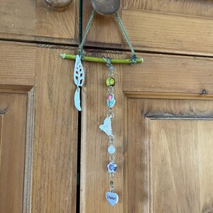 May include: A decorative hanging ornament with a twig, a white leaf, a butterfly charm, beads, and a heart charm that says "I bite!"