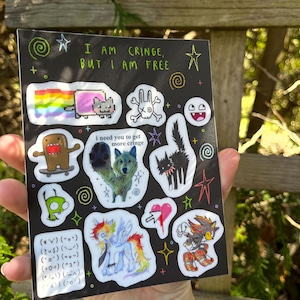 May include: Black sticker sheet with various colorful cartoon graphics. Includes a Nyan Cat, Domo, a wolf, a black cat, a pony, and other characters. Text reads "I AM CRINGE, BUT I AM FREE" and "i need you to get more cringe".