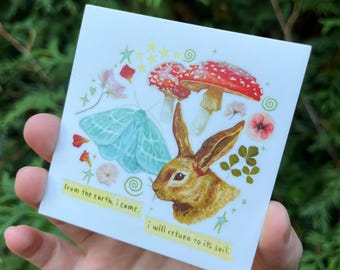 May include: Square sticker with a whimsical illustration featuring a brown rabbit, a blue moth, and red and white mushrooms. The sticker has text that reads "from the earth, I came. I will return to its soil."