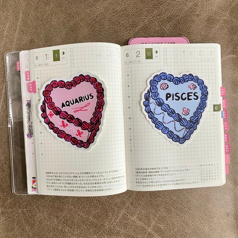 May include: Two heart-shaped stickers with astrological signs. The sticker on the left is pink with the sign Aquarius. The sticker on the right is blue with the sign Pisces.