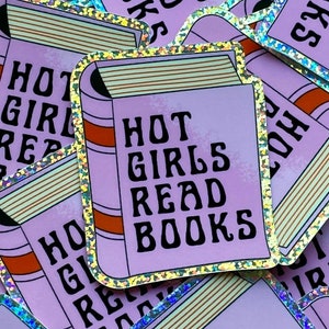 Könnte beinhalten: Ein lilafarbener Aufkleber mit glitzerndem Rand und dem Text "HOT GIRLS READ BOOKS" in einer stilisierten Schrift. Der Aufkleber ist in Form eines Buches mit einem Rücken und Seiten gestaltet.