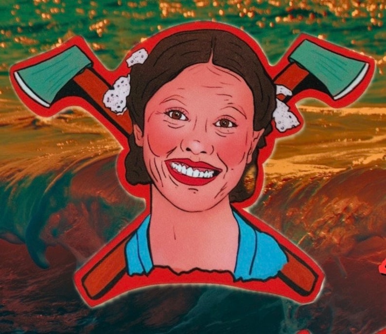 May include: A red, white, and blue sticker with a cartoon image of a woman with a big smile. She has two crossed axes behind her head. The background is a blurry image of water.