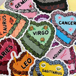 May include: A set of 10 colorful heart-shaped stickers featuring the astrological signs: Gemini, Taurus, Aries, Virgo, Cancer, Aquarius, Leo, Sagittarius, Capricorn, and Pisces. Each sticker has a unique design with a cake theme.