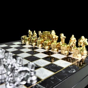 May include: A gold chess set with pieces in the shape of warriors and a castle. The pieces are arranged on a black and white chequered chessboard.