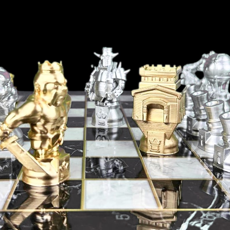 May include: A gold and silver chess set with a black and white marble board. The pieces are stylised and include a king, queen, knight, and rook. The board is set up for a game of chess.