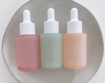 May include: Three frosted glass bottles with dropper tops. The bottles are pink, green, and peach.