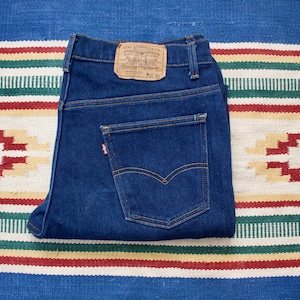 Op de afbeelding: Een paar blauwe spijkerbroeken gevouwen in de helft. De spijkerbroek heeft een bruin leren patch met de tekst "Levi Strauss & Co. San Francisco, Cal.  W.R.  U.S.A.  Pat.  No.  701,559" op de achterkant.