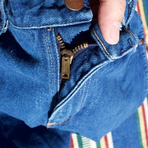 May include: A pair of blue denim jeans with a zipper and a metal button. The zipper has the word "SCOVILL" printed on it.