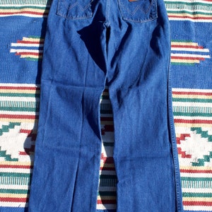 May include: A pair of dark blue denim jeans with a leather patch on the back pocket that says "Wrangler".