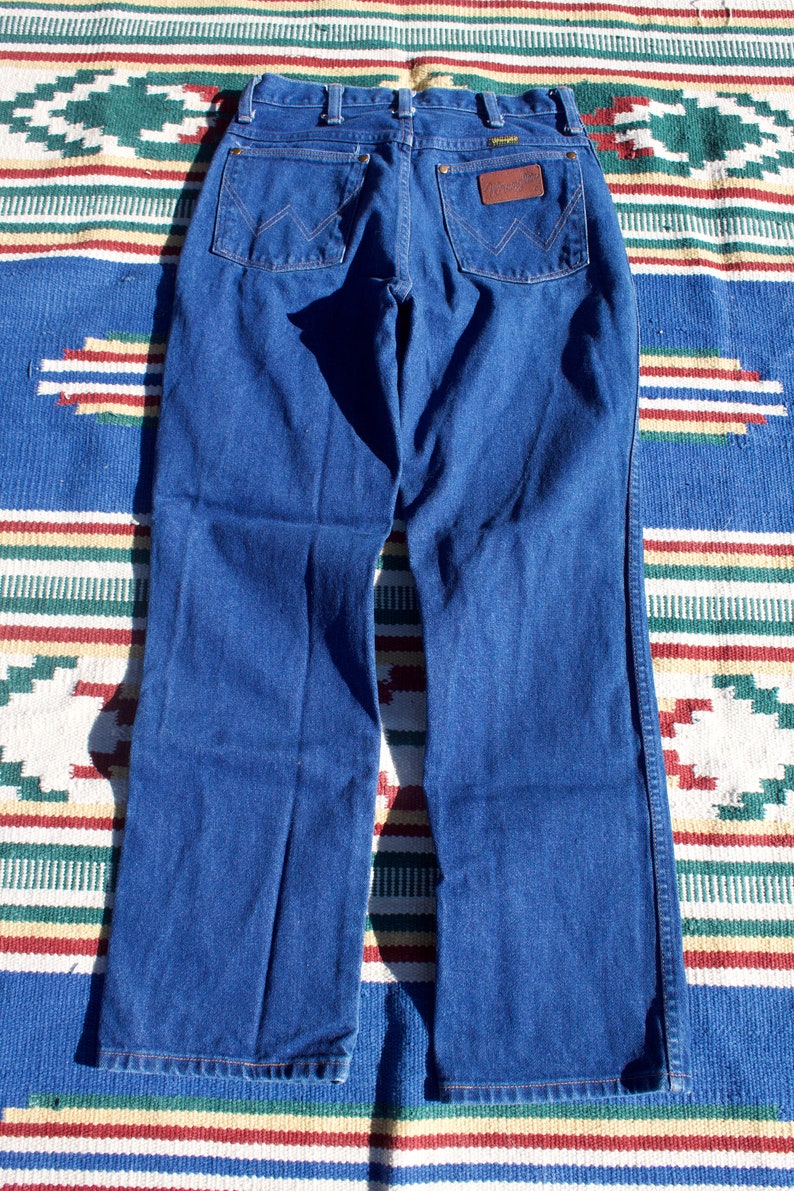 May include: A pair of dark blue denim jeans with a leather patch on the back pocket that says "Wrangler".