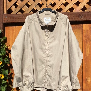 May include: A tan jacket with a full zipper closure and a collared neckline. The jacket has long sleeves with buttoned cuffs. The label on the inside of the collar reads "UNITED FOX". The jacket is hanging on a black hanger.