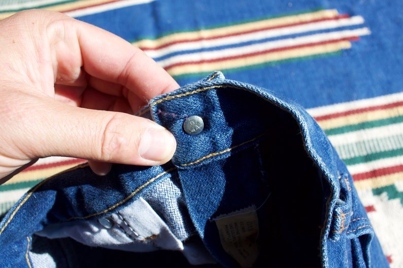 May include: Close-up of the inside of a pair of blue denim jeans showing the top button and waistband. The jeans are turned inside out.
