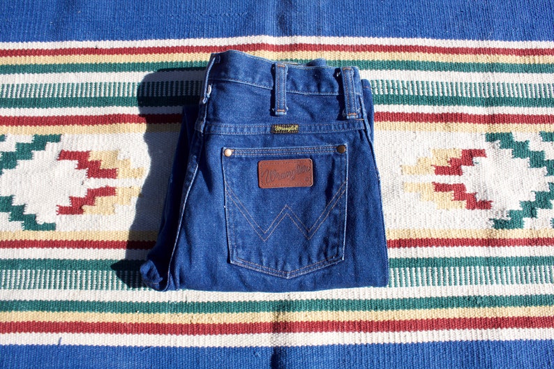 May include: A pair of blue denim jeans with a brown leather patch that says "Wrangler" on the back pocket.