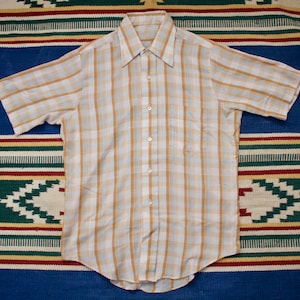 Könnte beinhalten: Ein kurzärmeliges Hemd mit Knöpfen in hellbrauner und weißer Karomuster mit Kragen.