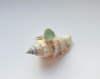 May include: A silver ring with a light green sea glass stone set on a seashell.