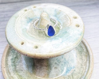 May include: A silver ring with a twisted band and a blue teardrop-shaped sea glass stone.