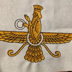 May include: An embroidered Faravahar symbol on a light-colored fabric. The design features a central figure in gold thread with a white ring, flanked by two large, detailed gold wings and a tail, all outlined in black thread stitching.
