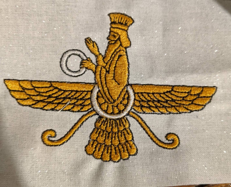 May include: An embroidered Faravahar symbol on a light-colored fabric. The design features a central figure in gold thread with a white ring, flanked by two large, detailed gold wings and a tail, all outlined in black thread stitching.