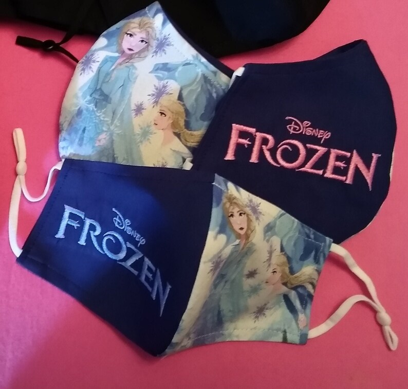 Pu&ograve; includere: Tre maschere in tessuto blu con lacci elastici bianchi per le orecchie. Le maschere hanno uno sfondo bianco con un design Frozen e il testo "Disney Frozen" in ricamo rosa.
