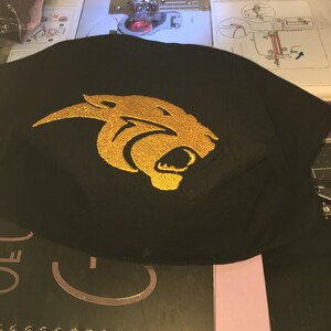 Pu&ograve; includere: Maschera facciale in tessuto nero con un design di testa di pantera ricamata in oro.