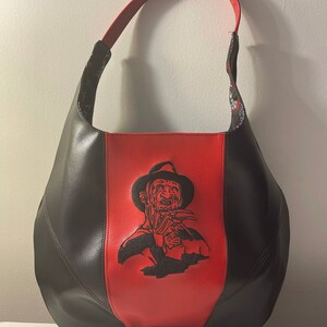 Pu&ograve; includere: Una borsa a mano in pelle nera e rossa con un'immagine ricamata nera di Freddy Krueger del film Nightmare on Elm Street.