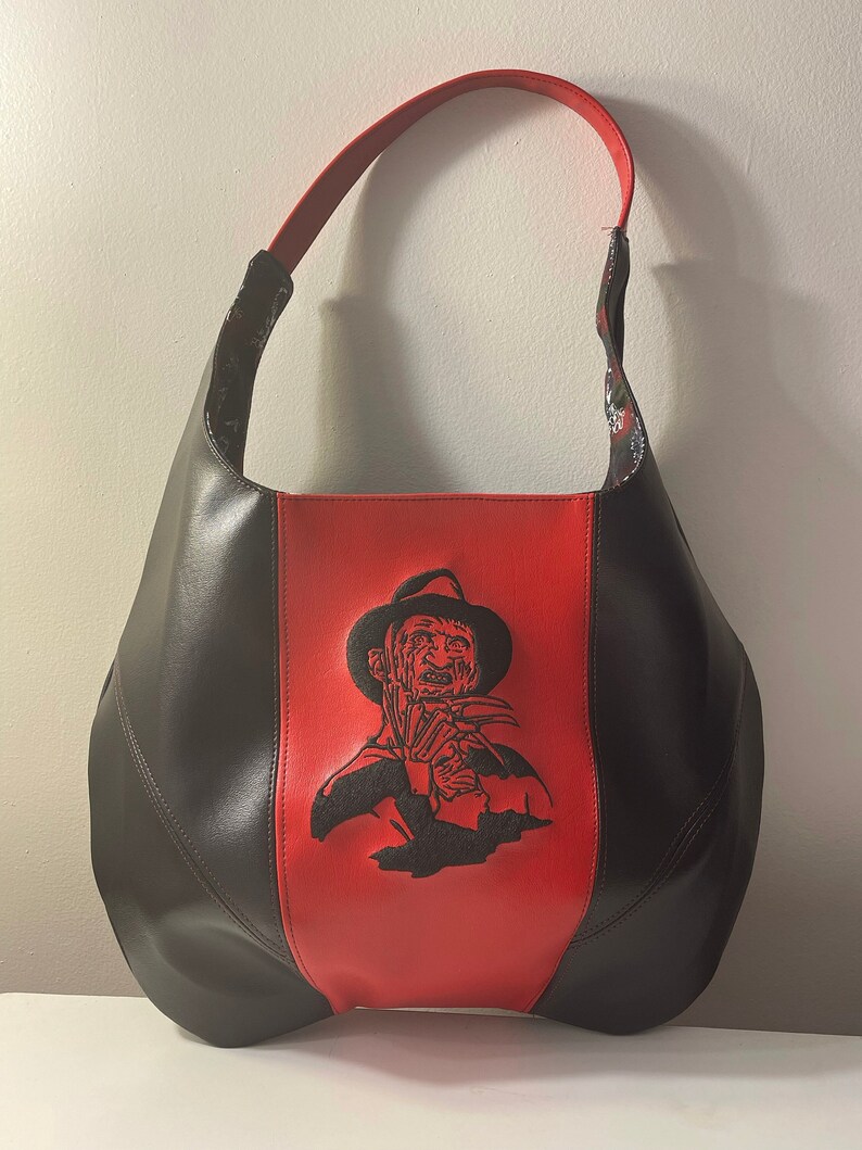 Pu&ograve; includere: Una borsa a mano in pelle nera e rossa con un'immagine ricamata nera di Freddy Krueger del film Nightmare on Elm Street.