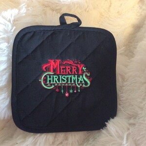 Pu&ograve; includere: Presa pentola imbottita nera con un ricamo rosso e verde "Buon Natale" con ornamenti appesi.