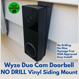 May include: A black Wyze Duo Cam doorbell mounted on vinyl siding with a white mount. The text "No Drilling No Glue Damage Free HOA Approved Easy Install!" is visible below the doorbell.