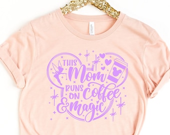 Może przedstawiać: Różowy T-shirt z fioletowym nadrukiem graficznym, na którym widnieje napis "This Mom Runs on Coffee & Magic". Grafika zawiera kubek z kawą, serce, zamek i wróżkę.