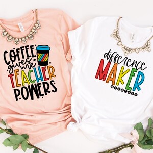 May include: Two t-shirts with rainbow text. The pink shirt says "Coffee gives me teacher powers" with a rainbow coffee cup graphic. The white shirt says "difference maker #teacher" in rainbow letters.