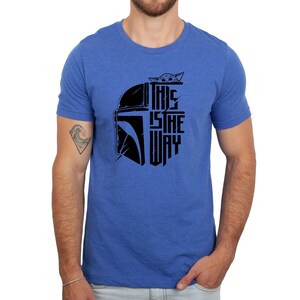 Puede incluir: Una camiseta azul real con un gr&aacute;fico negro de un casco mandaloriano y el texto "This is the way" con una peque&ntilde;a imagen de un personaje de la serie Star Wars, The Mandalorian, asom&aacute;ndose por la parte superior del casco.