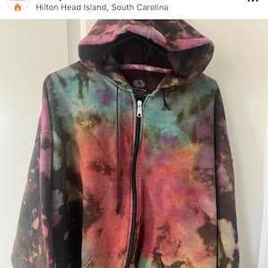 May include: A tie-dye zip-up hoodie with a black zipper and a black drawstring. The hoodie is a mix of red, orange, yellow, green, blue, purple, and black.