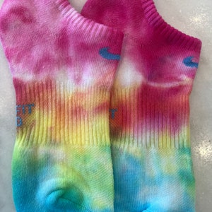 May include: A pair of tie-dye ankle socks in shades of pink, yellow, green, and blue. The socks have a white background with a tie-dye pattern.