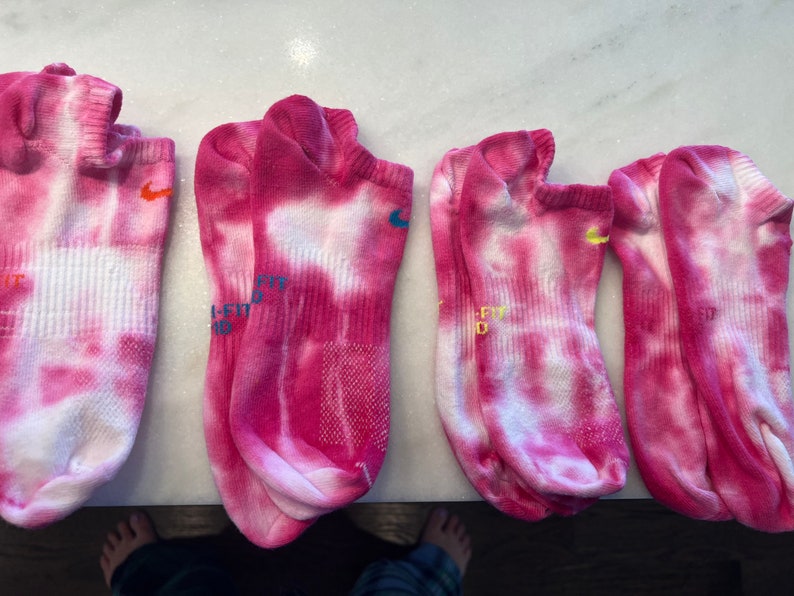 May include: Four pairs of pink and white tie-dye ankle socks with a Nike logo on each sock.
