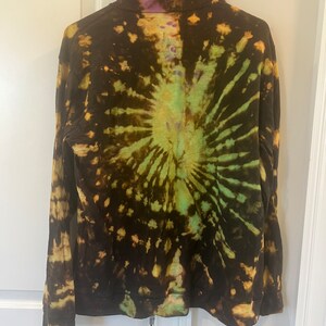 K&ouml;nnte beinhalten: Ein lang&auml;rmliger Kapuzenpullover mit einem Batik-Muster in den Farben Schwarz, Gr&uuml;n und Lila.