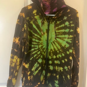 K&ouml;nnte beinhalten: Ein tie-dye Kapuzenpullover mit Rei&szlig;verschluss in Schwarz, Gr&uuml;n und Gelb.