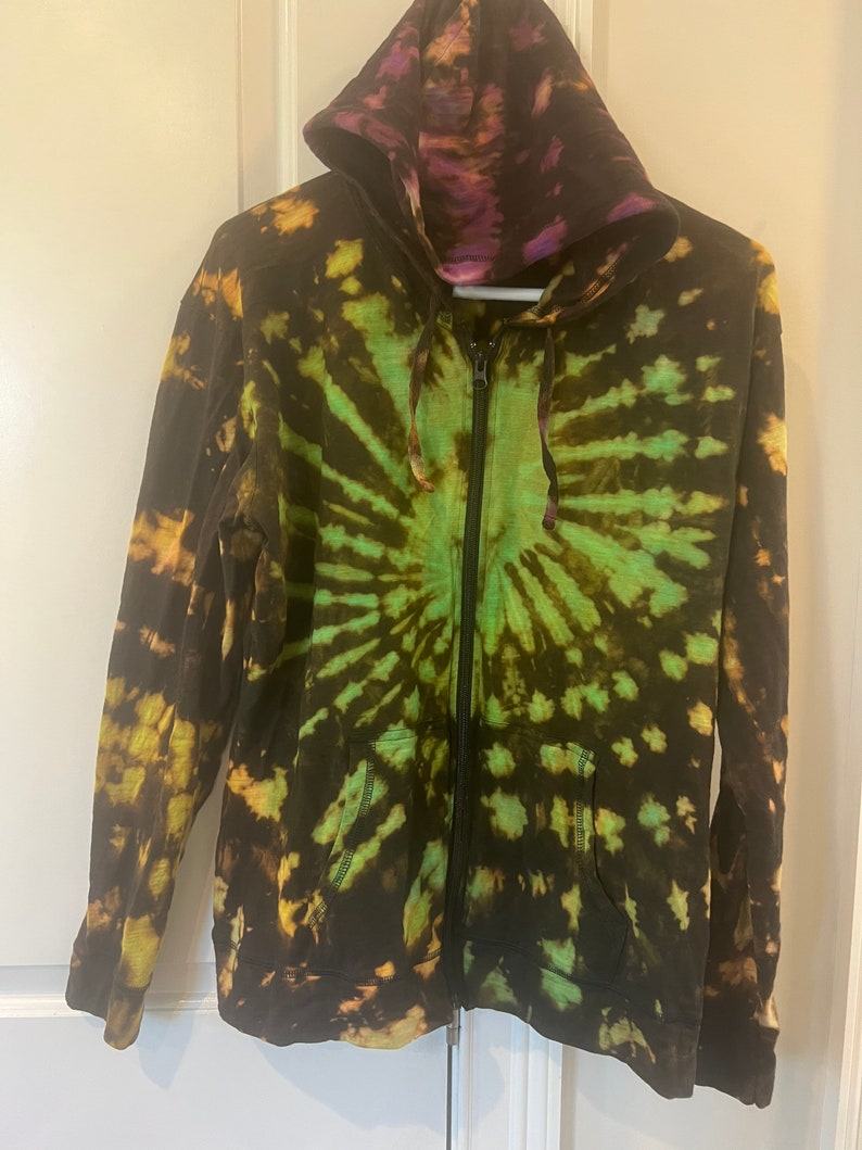 K&ouml;nnte beinhalten: Ein tie-dye Kapuzenpullover mit Rei&szlig;verschluss in Schwarz, Gr&uuml;n und Gelb.