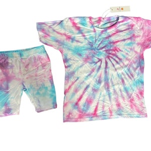 May include: A tie-dye shirt and shorts set in shades of pink, blue and white. The shirt has a round neckline and short sleeves. The shorts are biker shorts with an elasticated waistband.